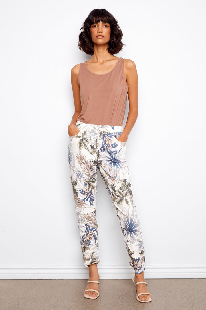 Woman wearing a beige tank top and floral pants against a white background