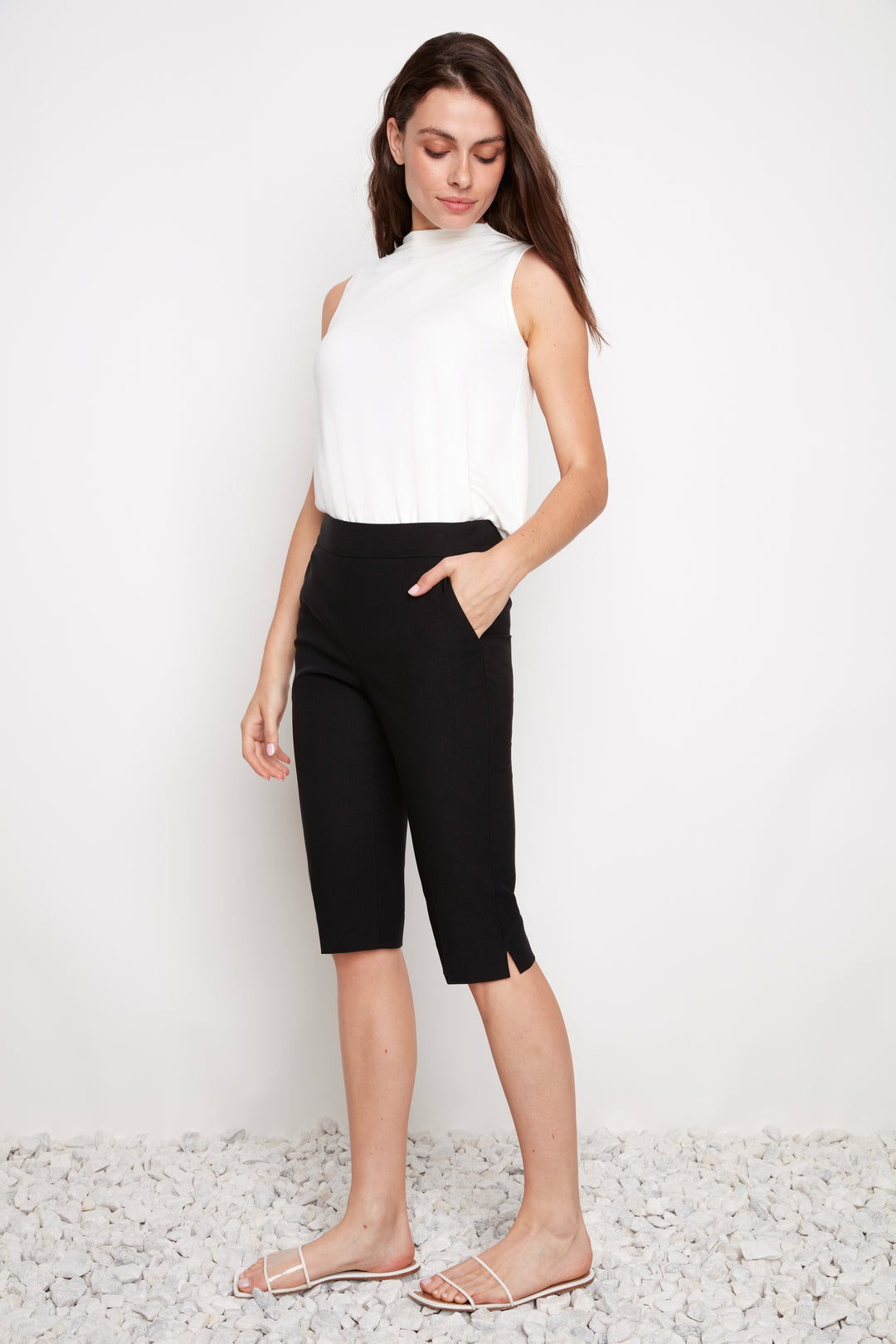 Woman wearing a white sleeveless top and black shorts against a white background
