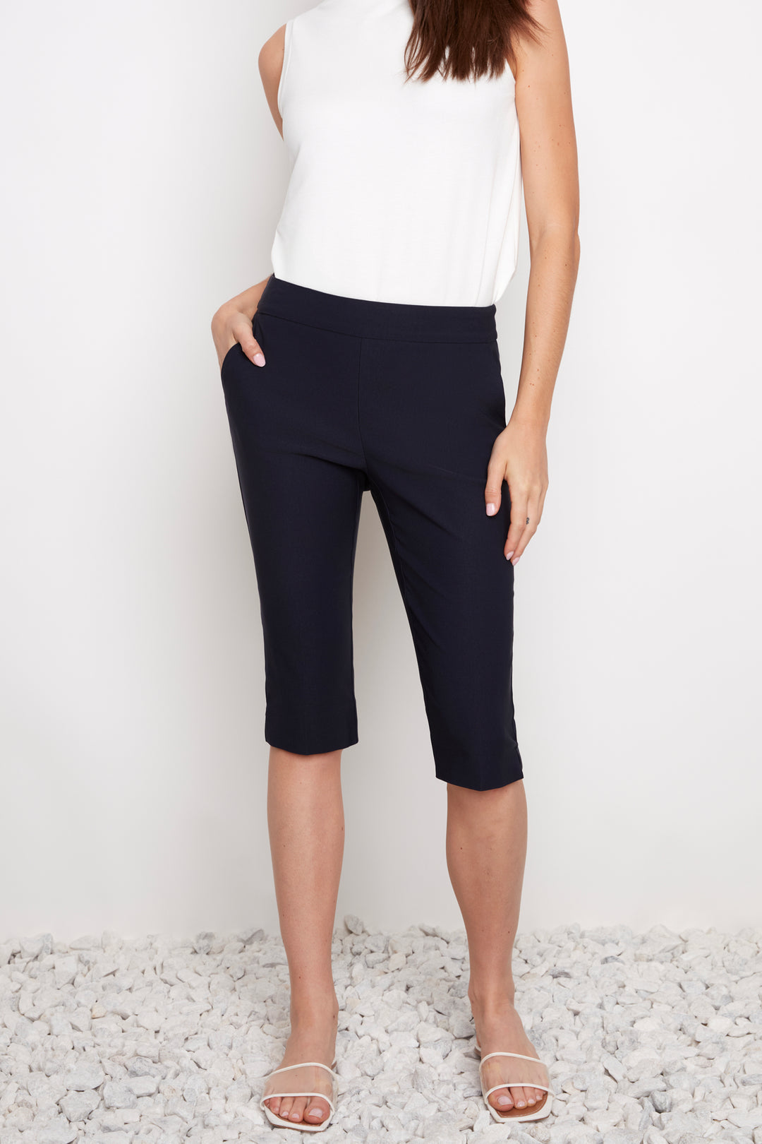 Person wearing navy capri pants and a white top on a light background