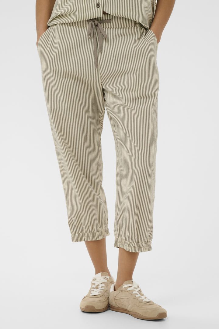 Person wearing beige striped  jogger pants and white sneakers on a white background