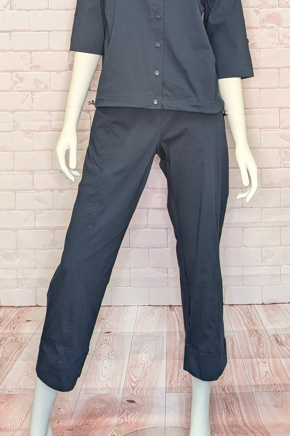 Mannequin wearing a black cargo style crop pant with a shirt and pants against a brick wall.