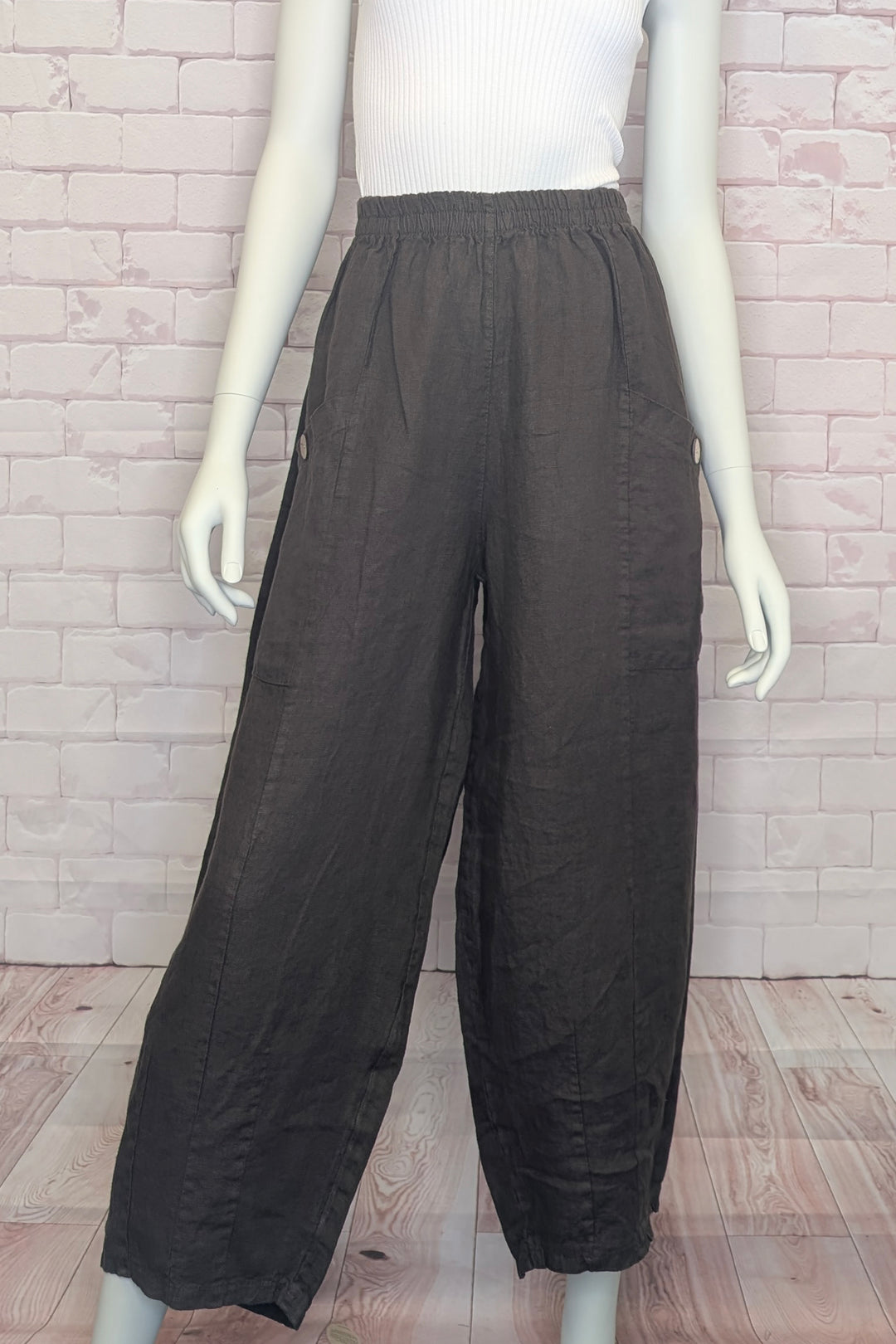 Mannequin wearing brown wide-leg pants against a brick wall.