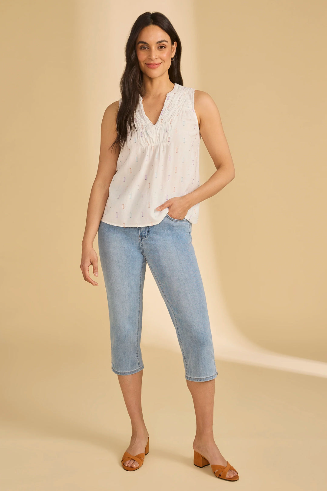 Woman wearing a white sleeveless top and light blue jeans on a beige background