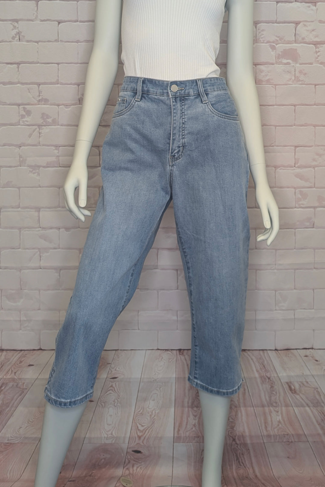 Mannequin wearing light blue denim capris against a brick wall.