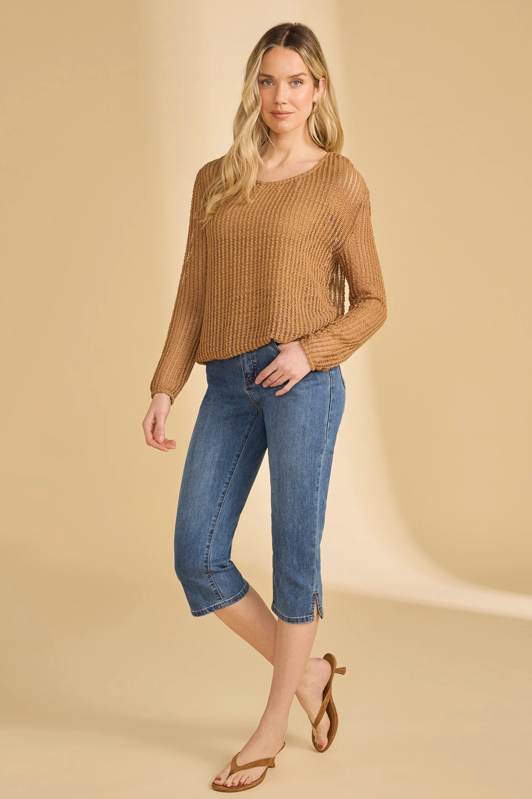 Woman wearing a brown ribbed sweater and blue jeans on a beige background
