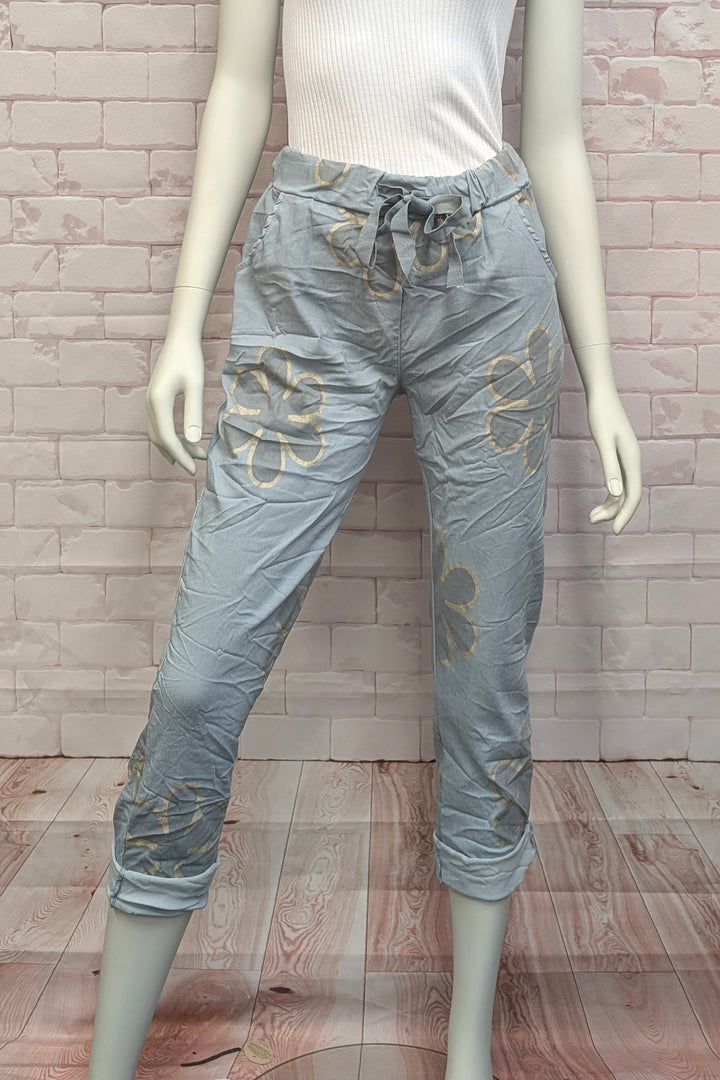 Mannequin wearing light blues crinkle joggers with daisy floral patterns against a brick wall.
