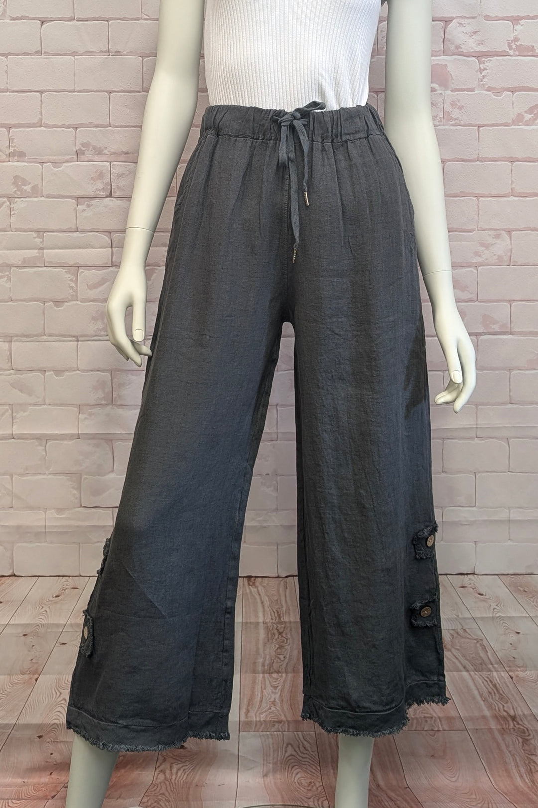 Mannequin wearing dark gray wide-leg linen pants with a white top against a brick wall.
