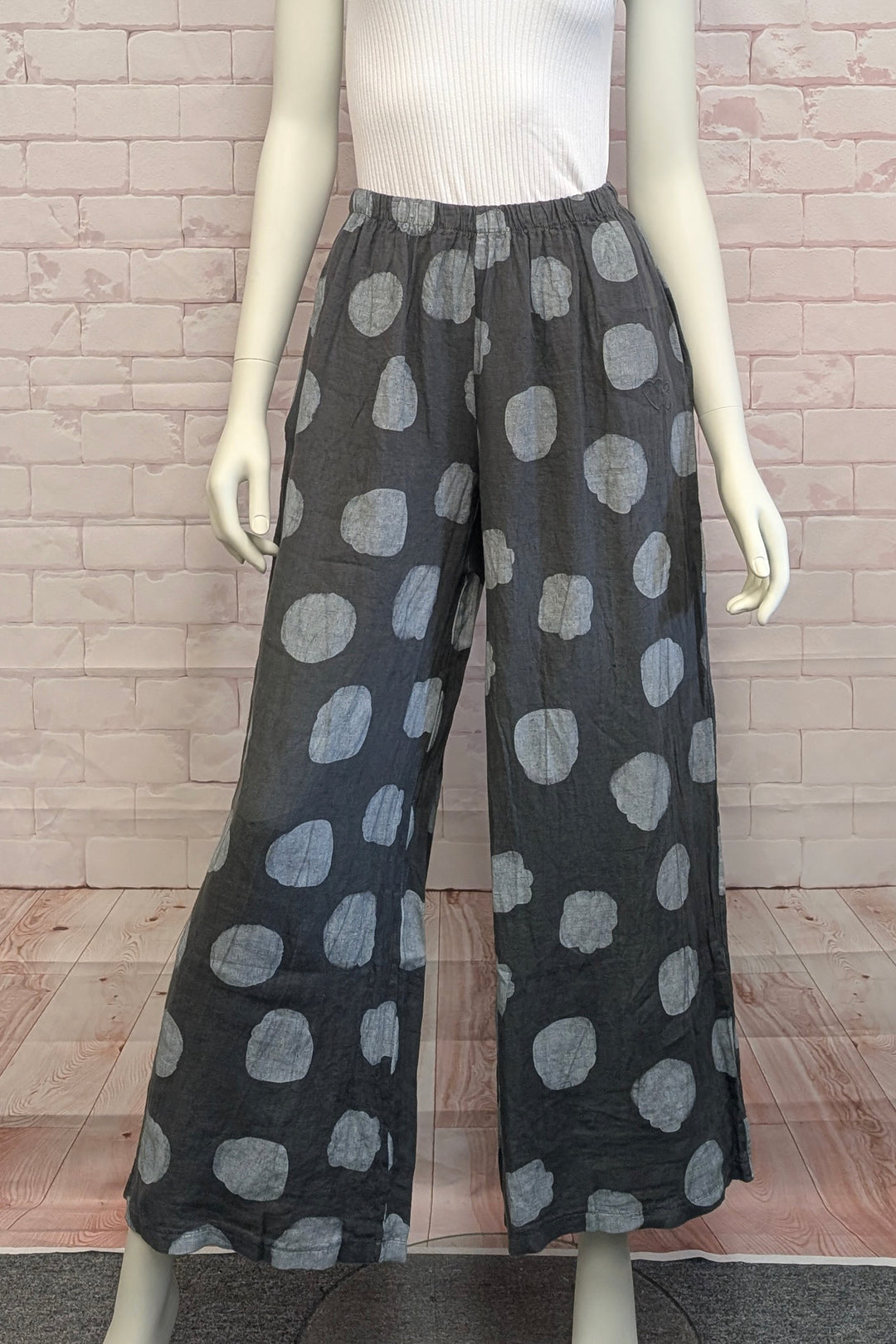 Mannequin wearing black pants with gray polka dots against a brick wall.