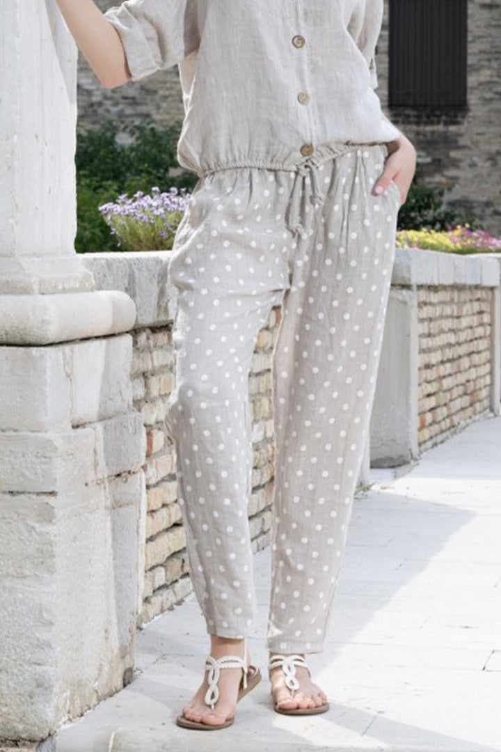Person wearing light-colored pants with a polka dot pattern, standing outdoors near stone walls and plants.