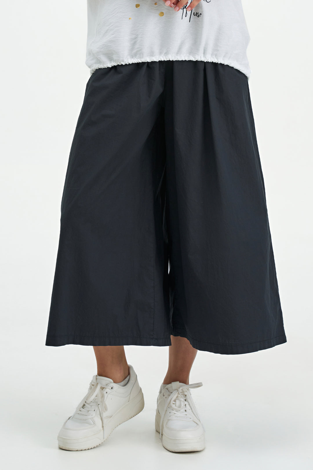 Person wearing black wide-leg cropped pants and white sneakers on a white background