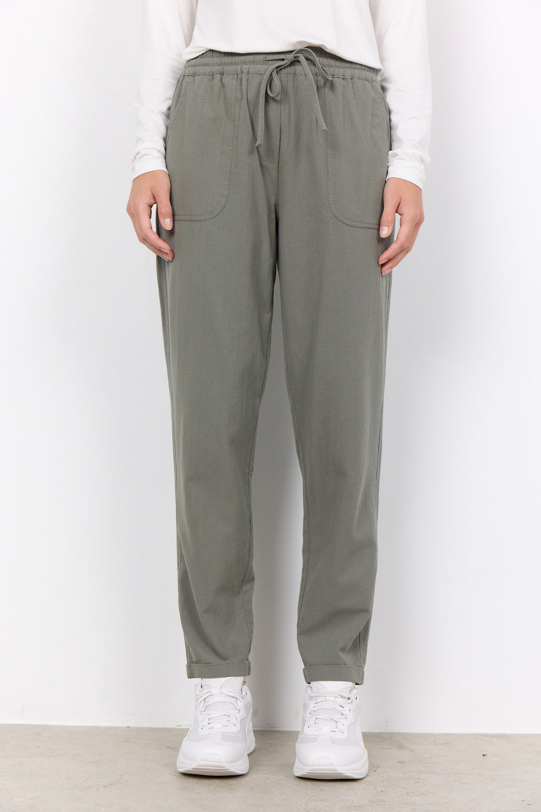 Person wearing gray jogger pants and white sneakers on a plain background