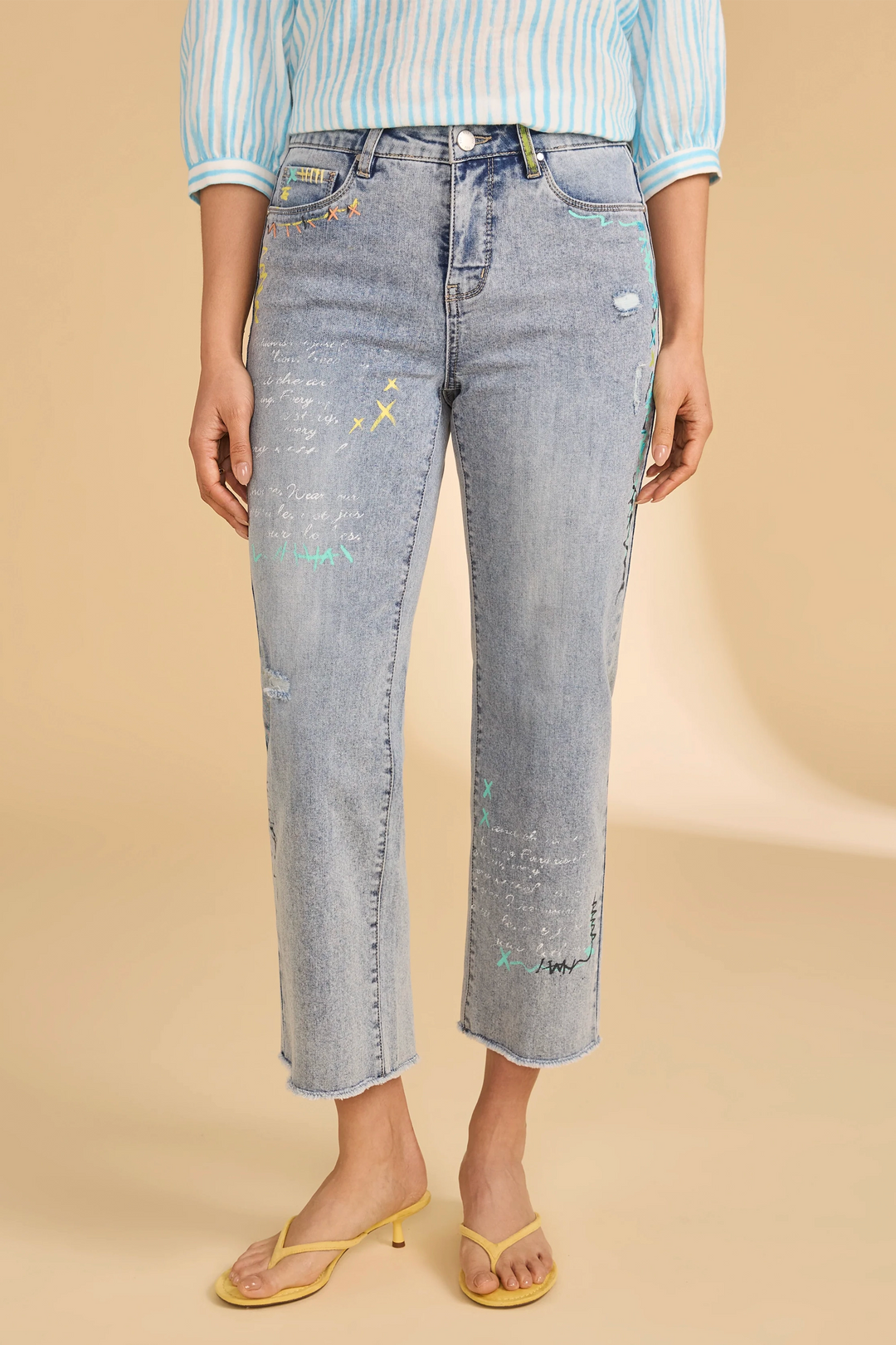 Person wearing light blue crop straight leg jeans with colorful scribble on a beige background
