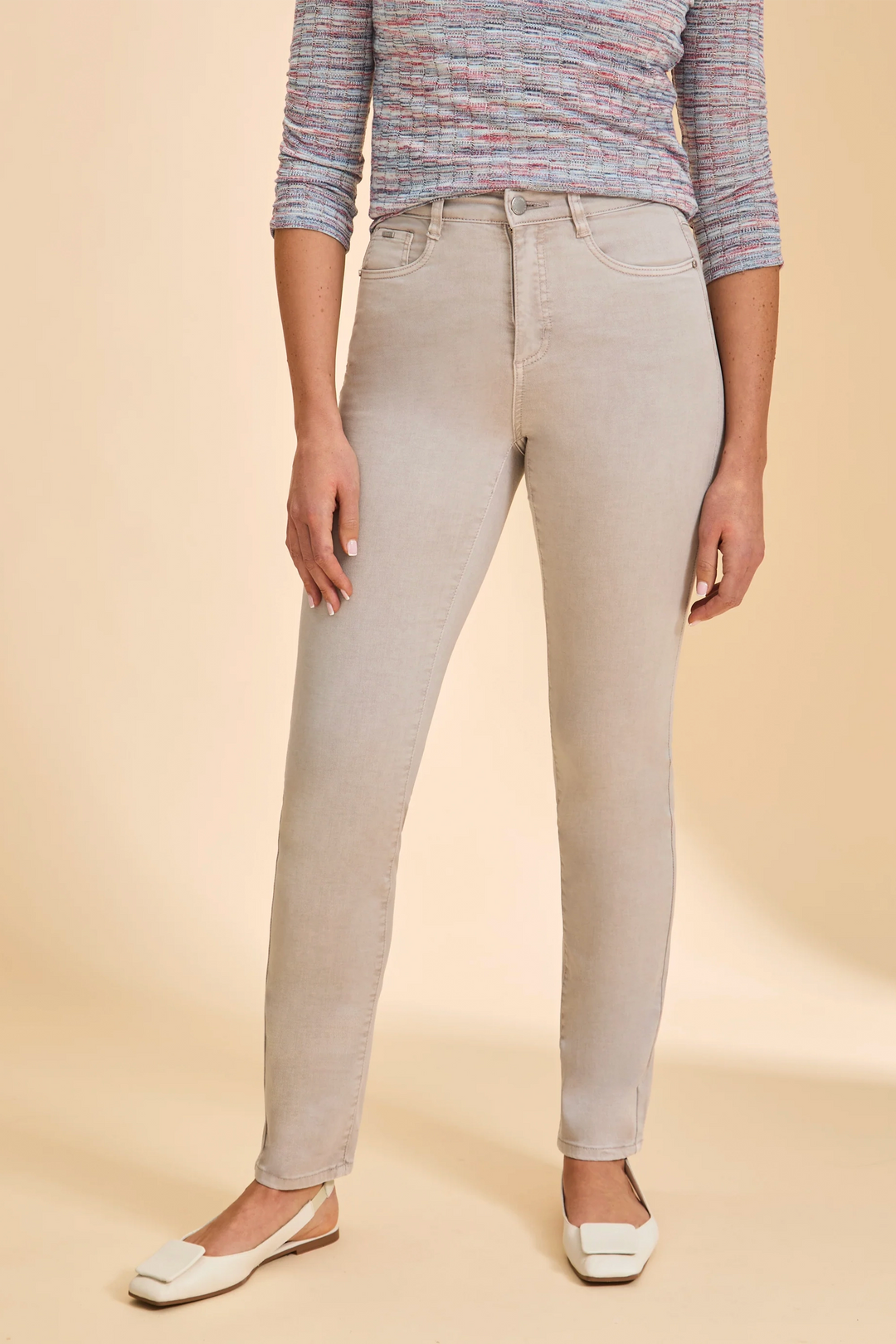 Person wearing beige slim leg jeans and a patterned top on a beige background