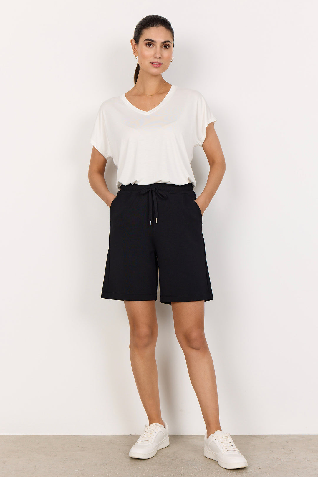 Person wearing black shorts with elastic waist and drawstring and a white top on a white background