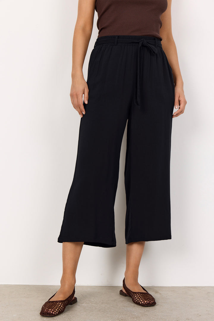 Person wearing black wide-leg pants with a brown top against a white background