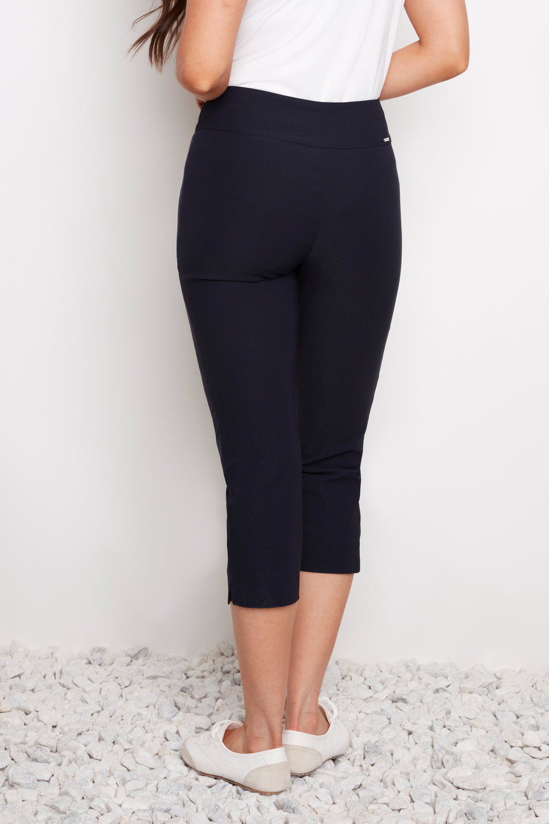 Person wearing navy capri pants and white shoes on a light gray background