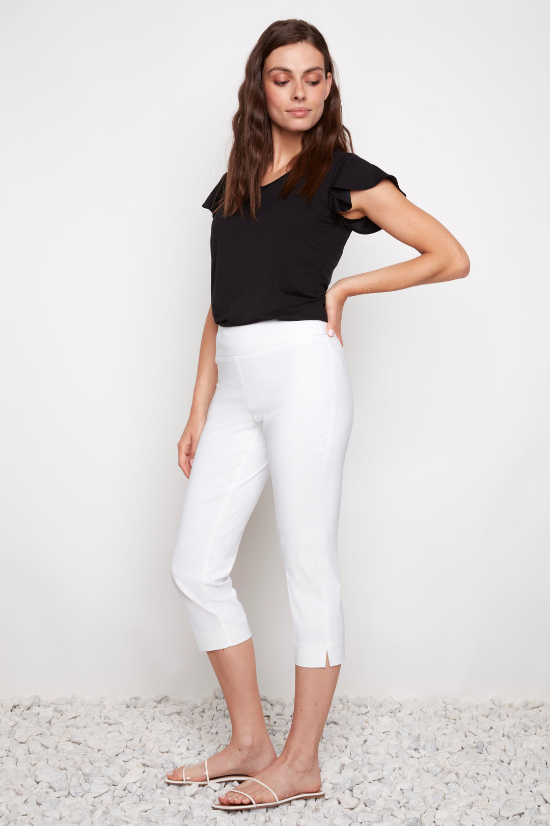 Woman wearing a black top and white capri pants against a white background