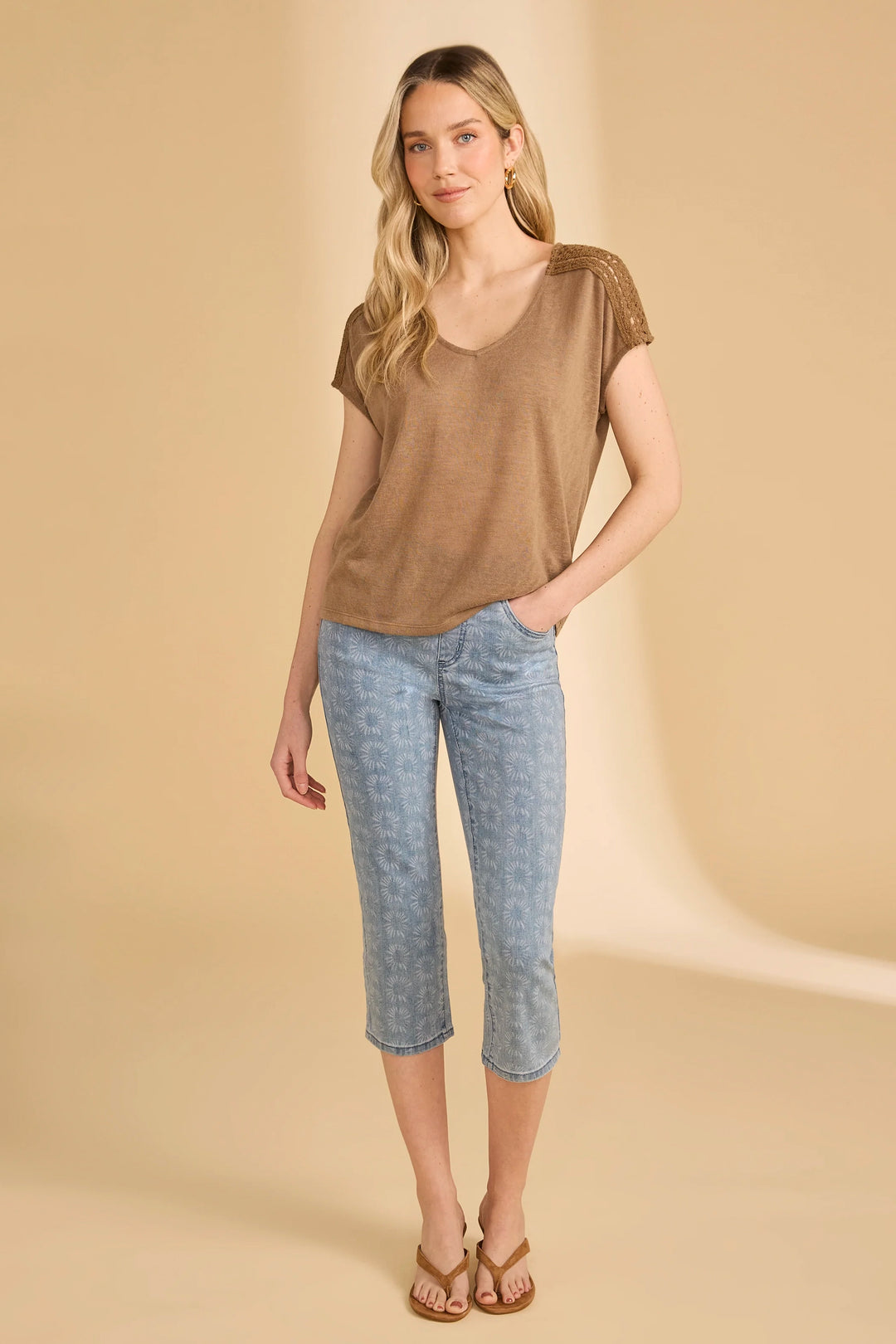 Woman wearing a brown top and light blue patterned pants on a beige background