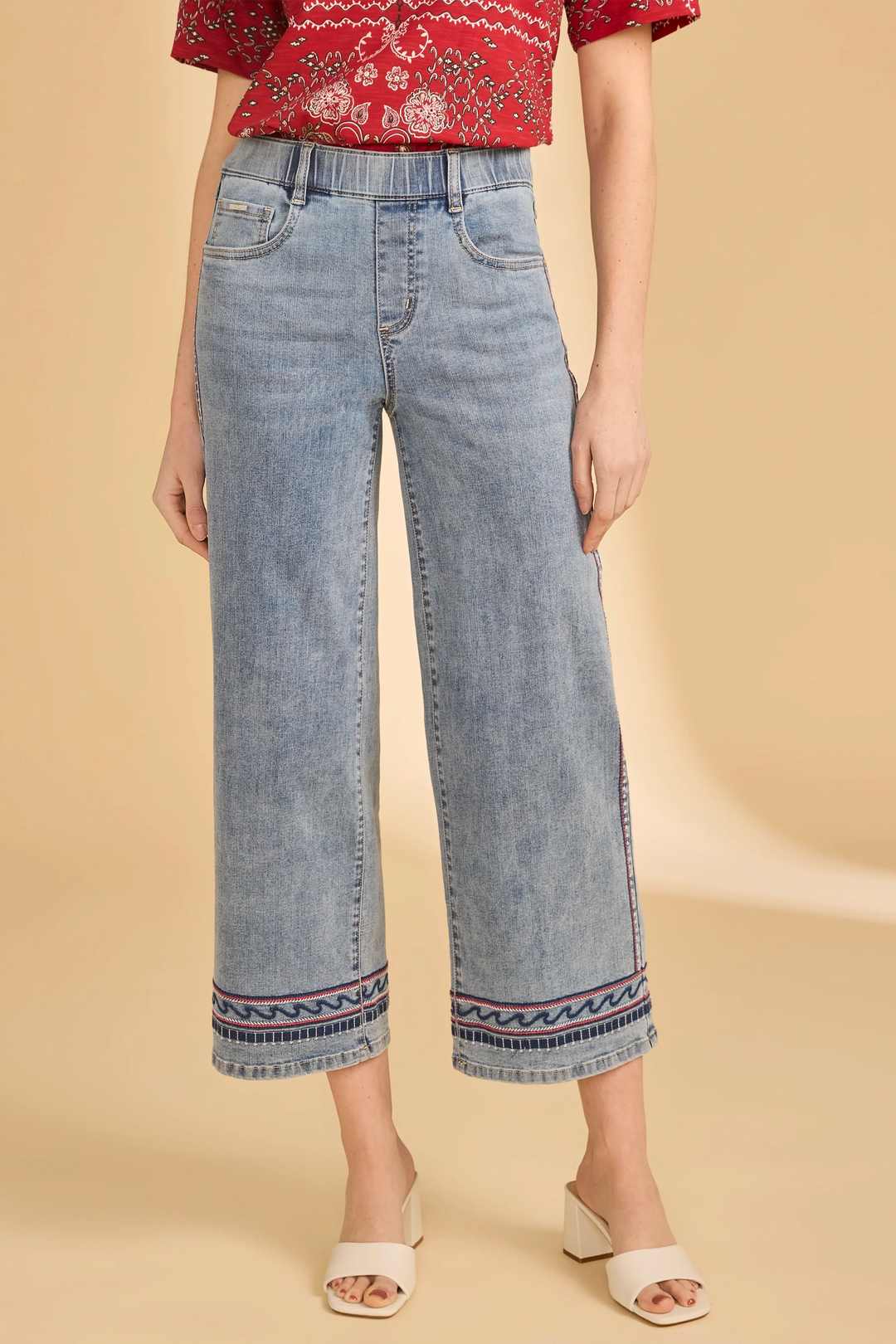 Person wearing blue jeans with decorative hem on a beige background