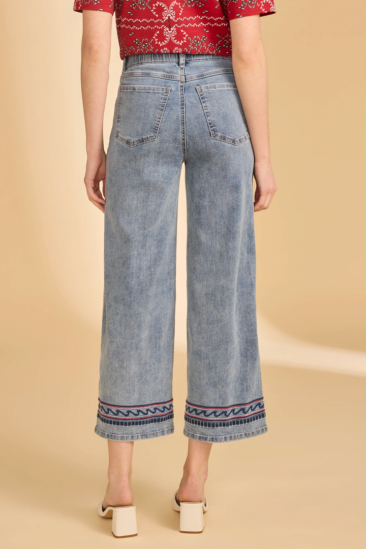 Person wearing light blue jeans with decorative hem on a beige background