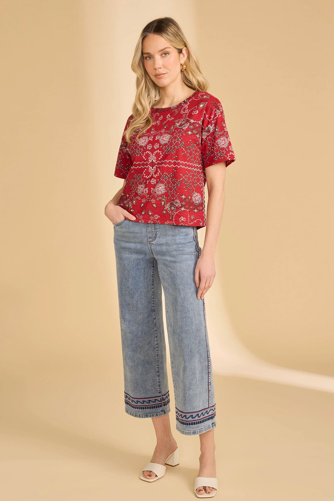 Woman wearing a red patterned top and blue jeans on a beige background