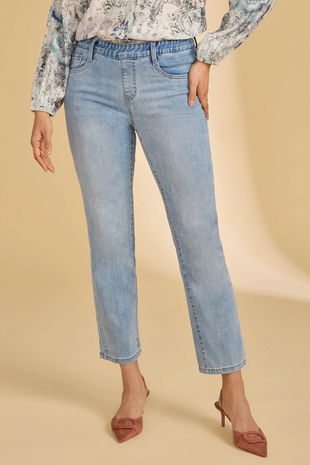 Person wearing light blue jeans and a patterned top on a beige background