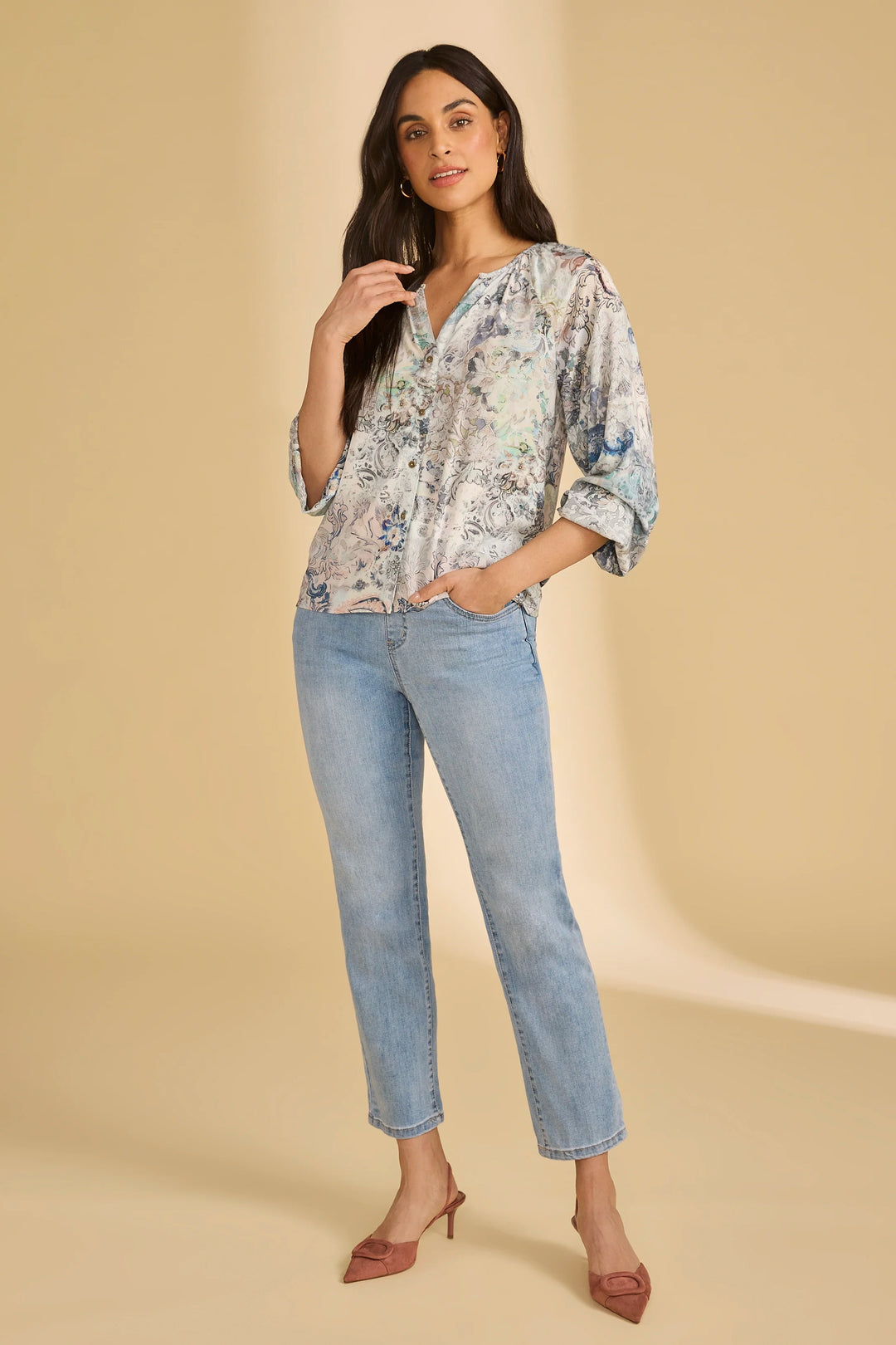Woman wearing a floral blouse and light blue jeans on a beige background