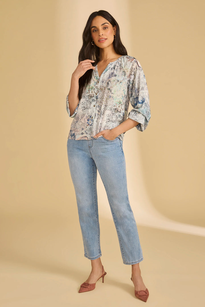 Woman wearing a floral blouse and light blue jeans on a beige background