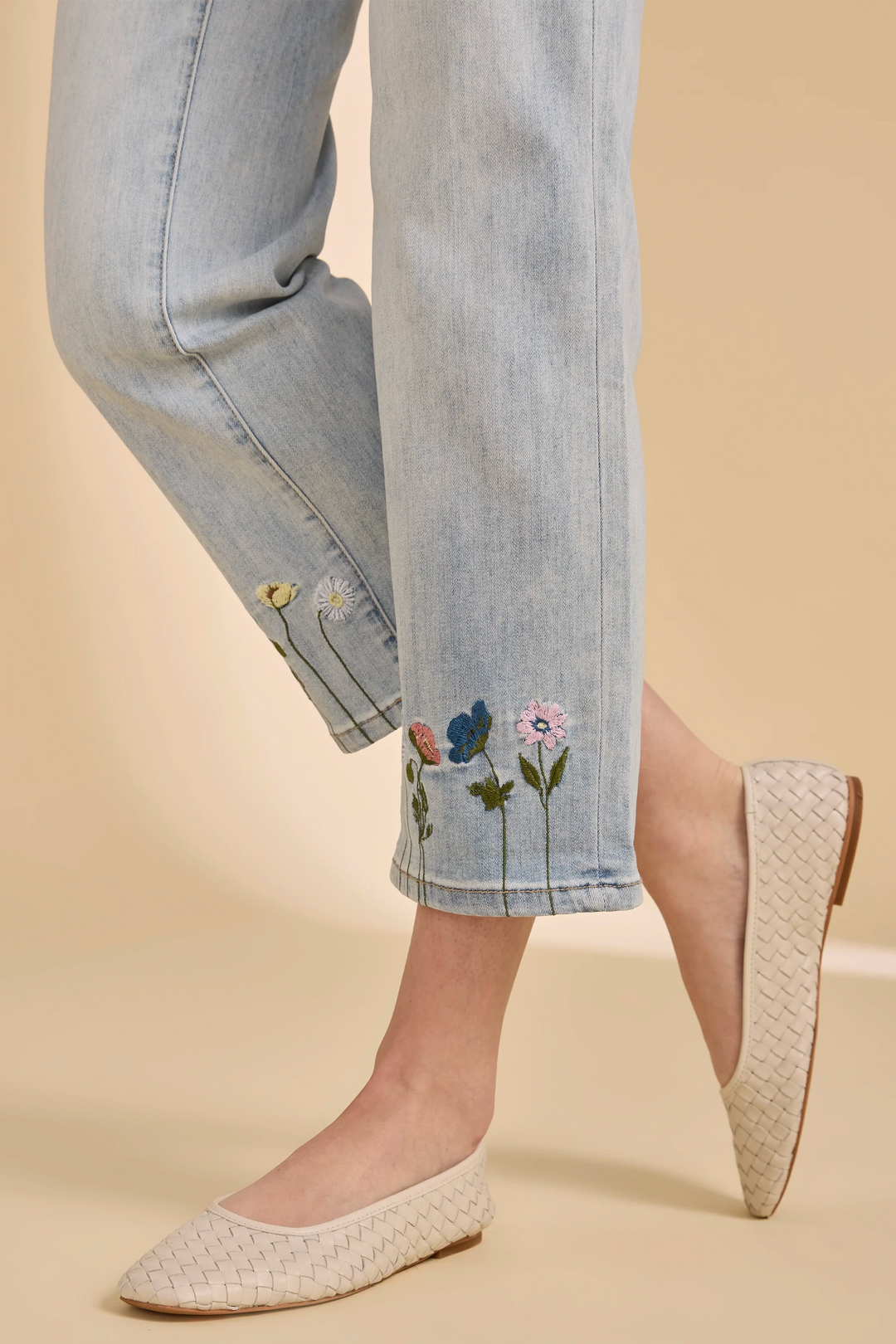 Denim pants with floral embroidery and beige flats on a beige background