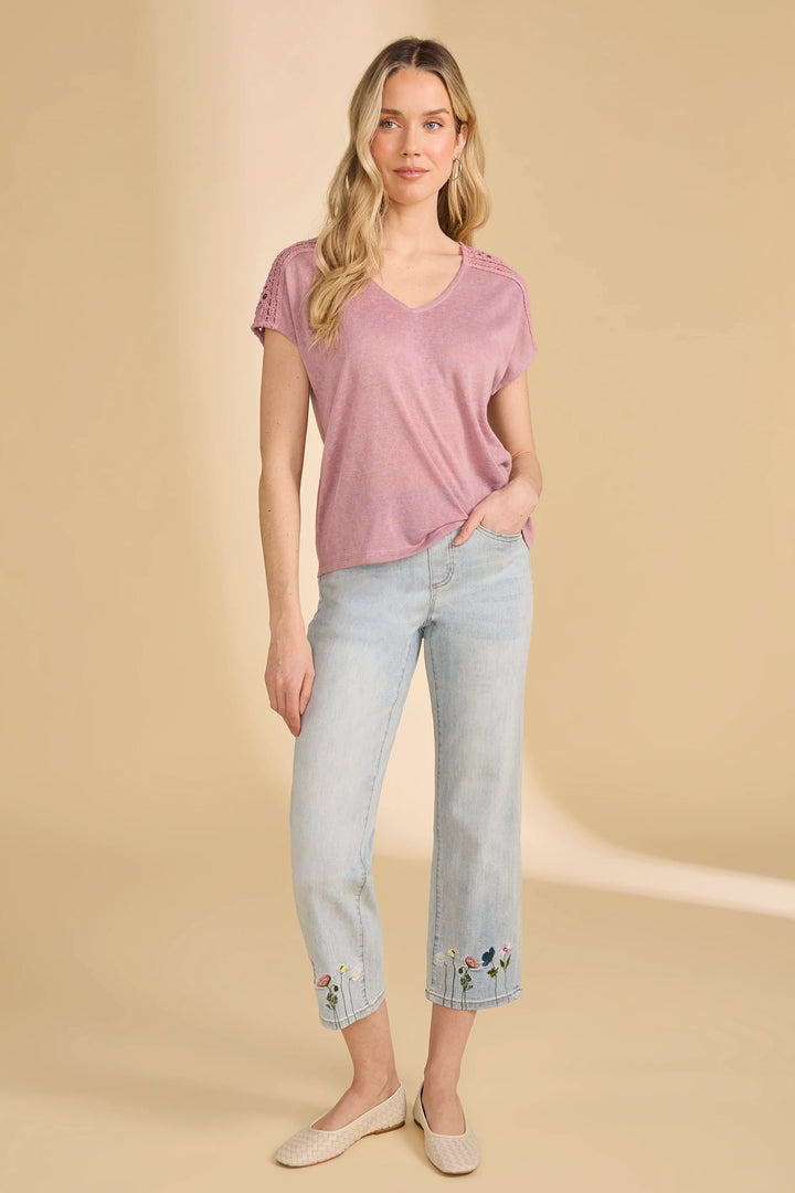 Woman wearing a pink top and light blue jeans with floral embroidery on a beige background
