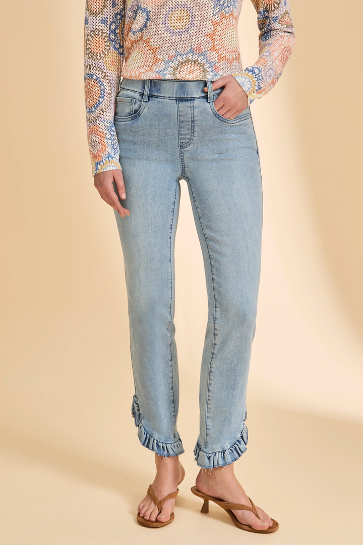 Person wearing light blue jeans and a patterned top on a beige background