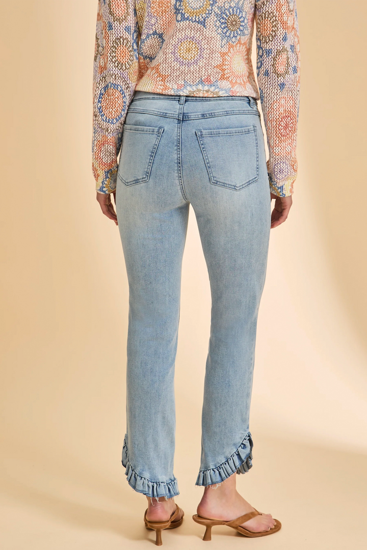 Person wearing light blue jeans with ruffled cuffs on a beige background