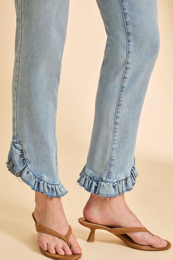 Close-up of blue jeans with ruffled cuffs worn by a person on a beige background