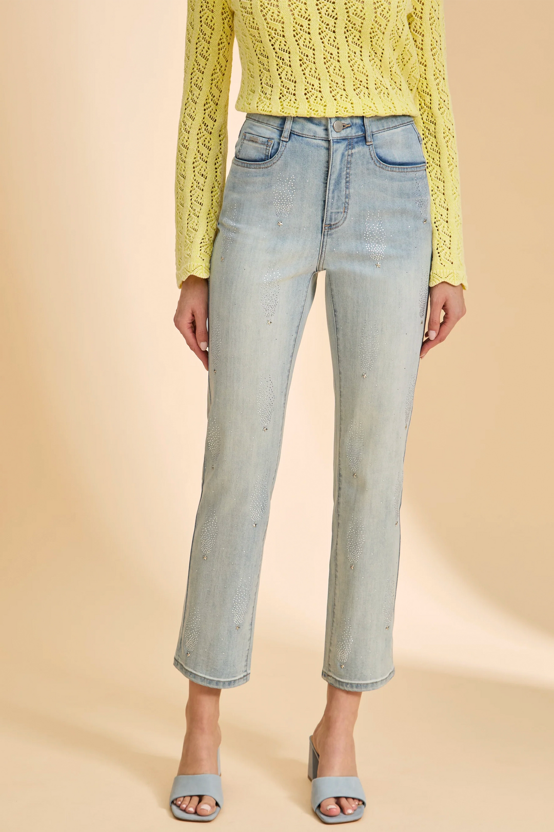 Person wearing a yellow knit sweater and light blue jeans on a beige background