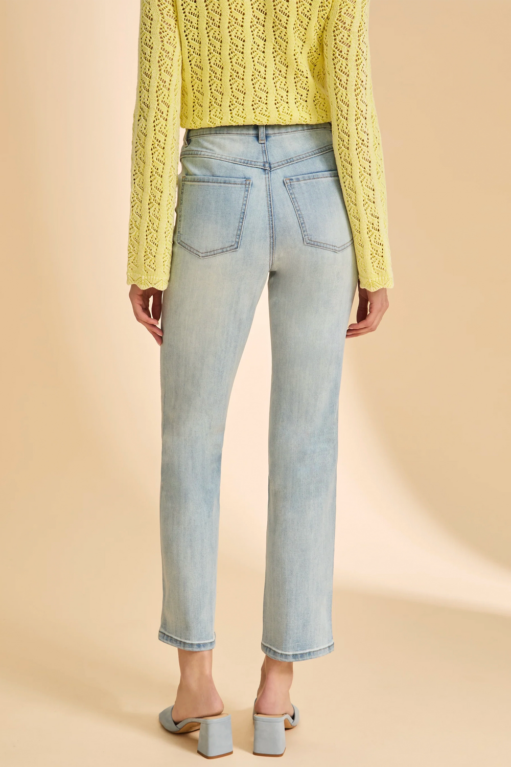 Person wearing light blue jeans and a yellow textured sweater on a beige background