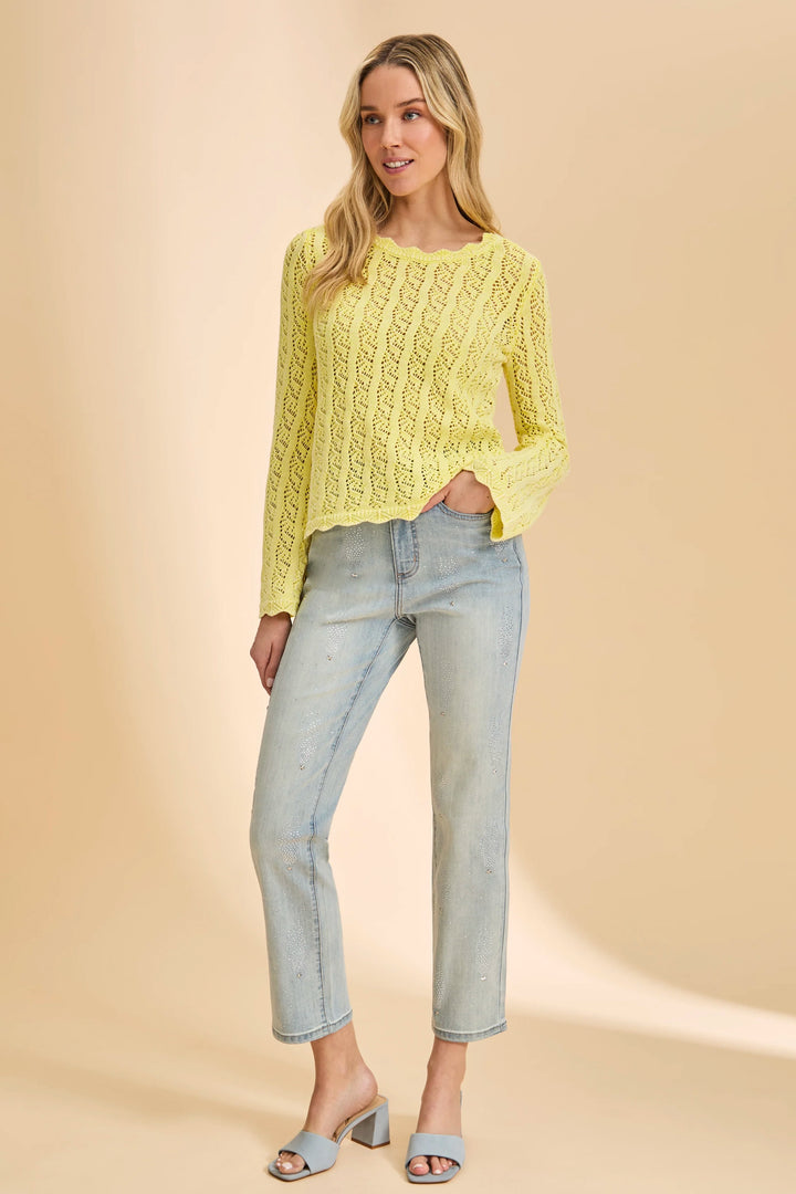 Woman wearing a yellow cable knit sweater and light blue jeans on a beige background