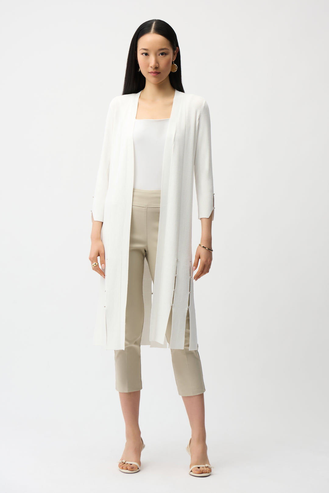 Woman wearing a white cardigan, white top, and beige pants on a white background