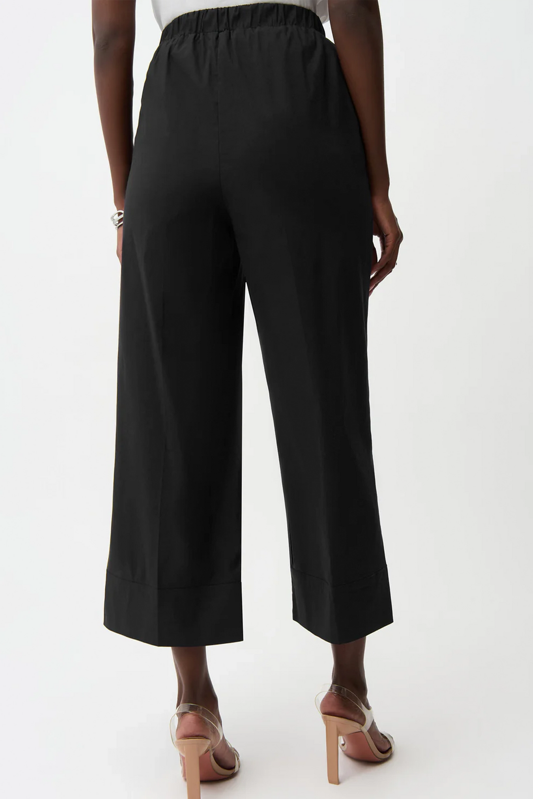 Black wide-leg cropped pants shown from the back on a model, paired with beige high-heeled sandals against a plain white studio background.