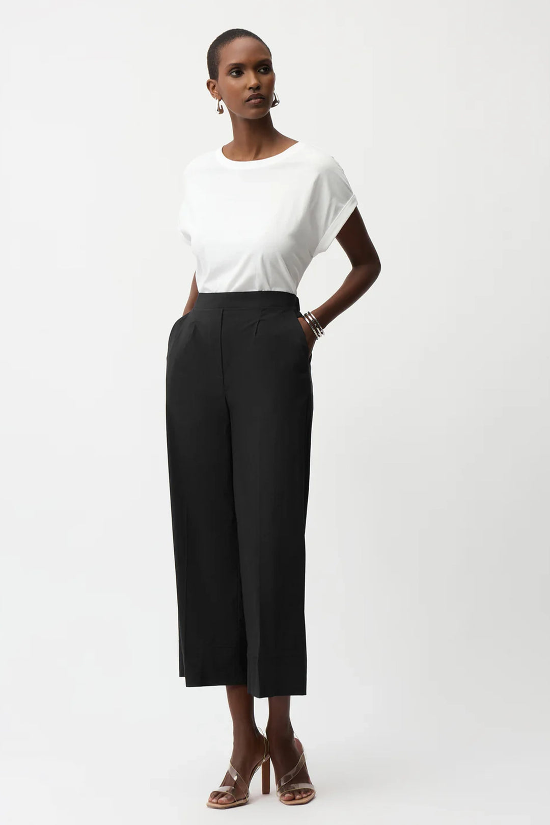 A model wearing a white short-sleeve crewneck top and black wide-leg cropped trousers, paired with brown heeled sandals, against a plain light gray studio background.
