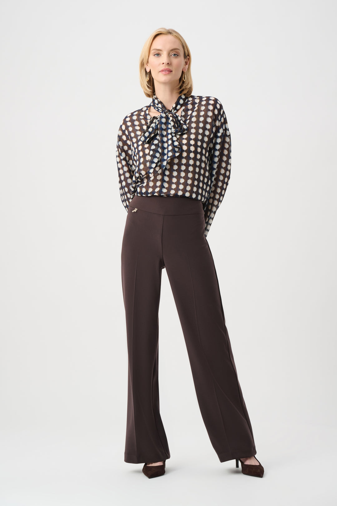 Woman wearing a patterned blouse and brown pants on a white background