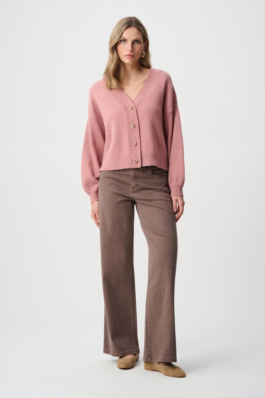 Woman wearing a pink cardigan and brown pants on a white background