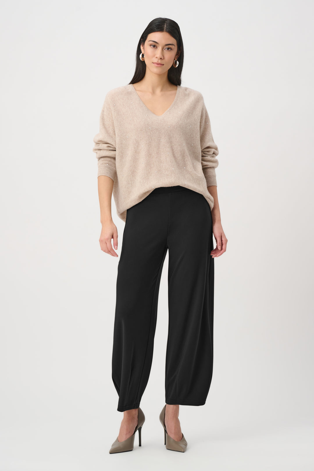 Woman wearing a beige sweater and black pants on a white background