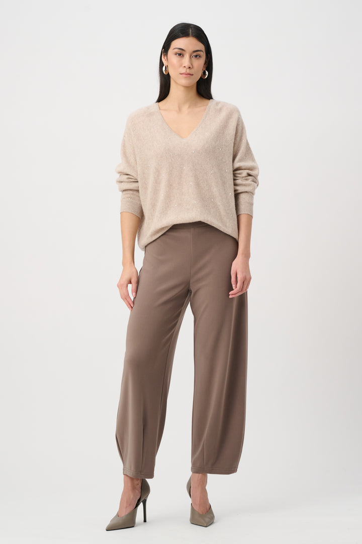 Woman wearing a beige sweater and brown pants on a white background