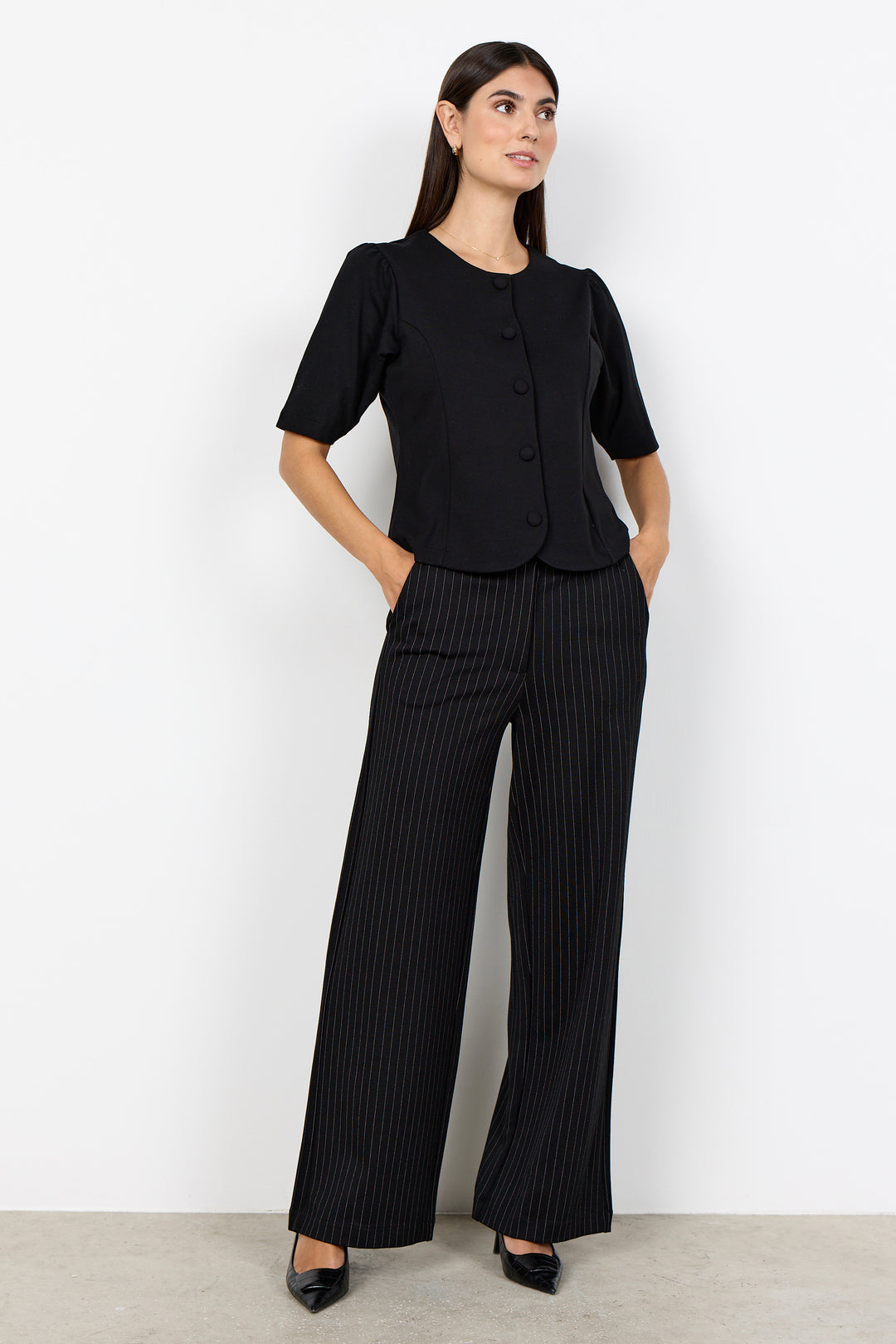 woman wearing a black blouse and black pinstripe wide leg pants on a white background. 