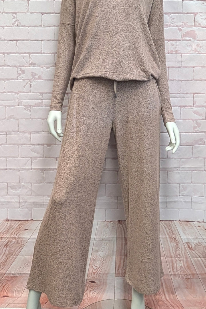 A two-piece knit loungewear set in a heathered taupe-brown color, featuring a long-sleeve top and matching wide-leg pants, displayed on a mannequin against a light brick wall and wood floor background.
