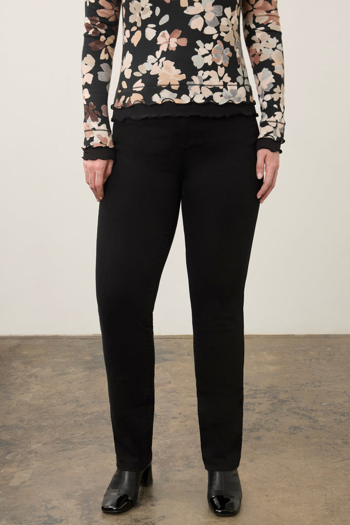 A model wearing black slim-fit trousers, paired with a black floral long-sleeve top and black leather ankle boots, standing against a neutral studio background.