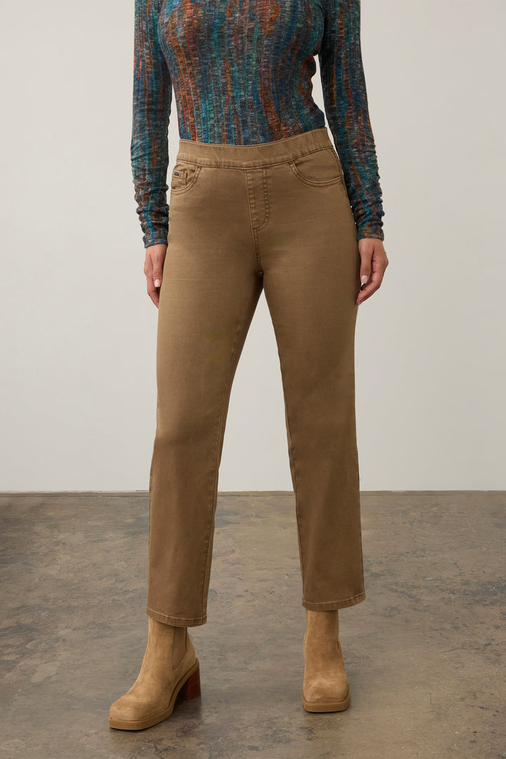 A model is shown from the chest down wearing straight-leg brown jeans, a patterned blue and orange long-sleeve top, and tan ankle boots against a neutral studio background.