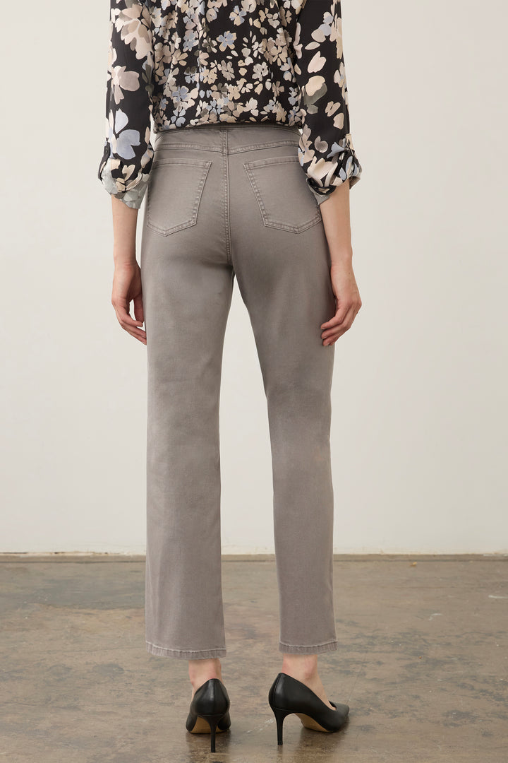 A person shown from the back wearing light gray cropped trousers, a black floral blouse, and black heels against a plain off-white wall and concrete floor.