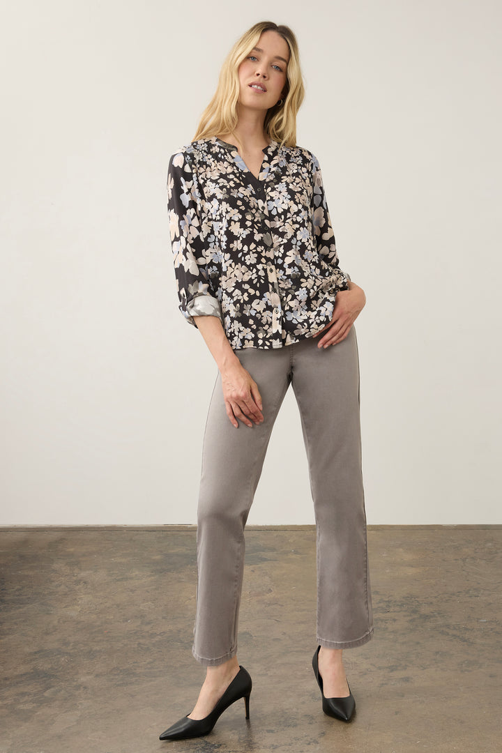 A woman modeling a black floral long-sleeve blouse with white and light pink flowers, paired with light gray straight-leg trousers and black pointed-toe heels, standing against a neutral studio backdrop.