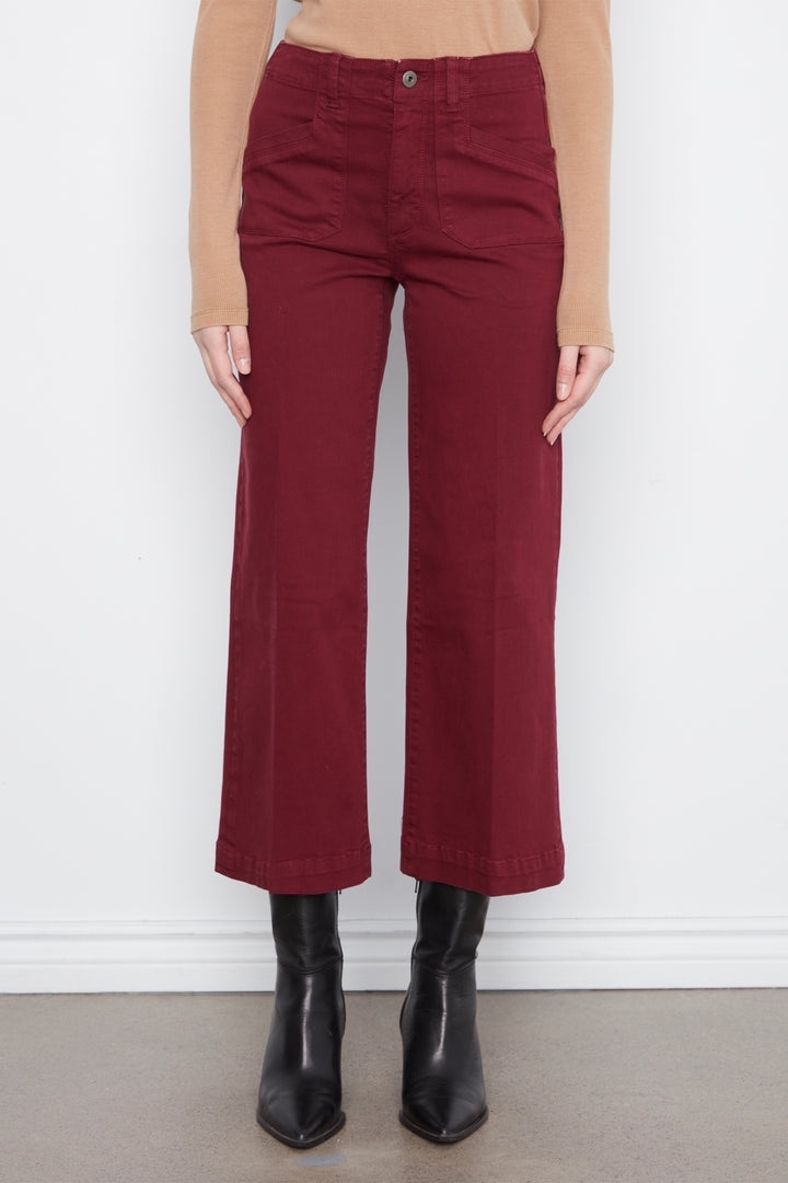 A model is shown from the waist down wearing a pair of high-waisted, wide-leg cropped pants in a deep burgundy color, styled with a beige long-sleeve top and black ankle boots.